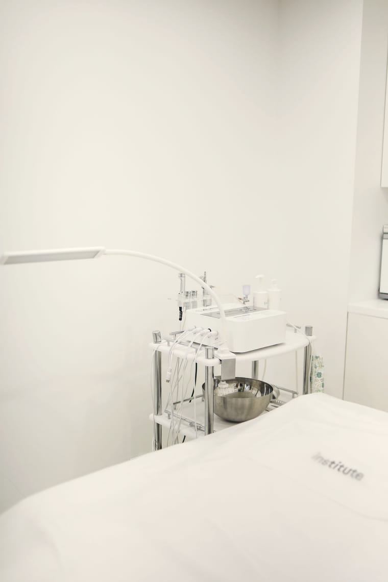 A clinic trolley holding treatment handpieces and supplies beside a prepared bed