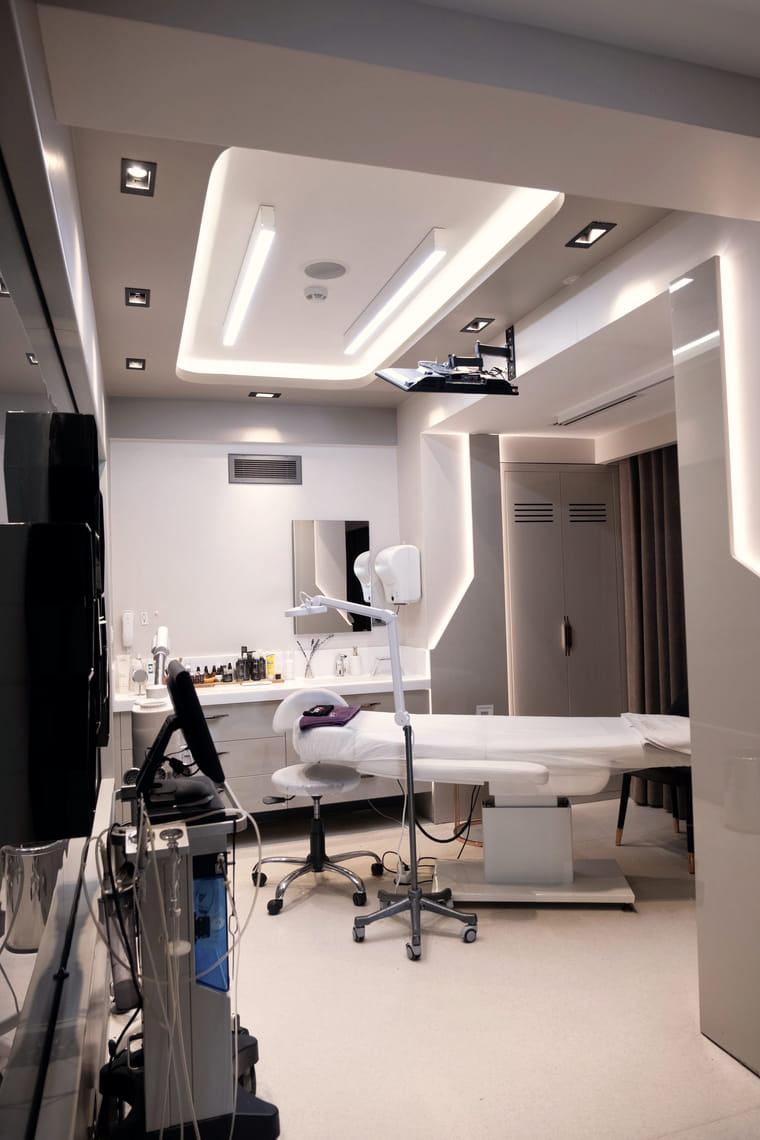 A modern treatment room with an adjustable bed, task lighting and equipment on a trolley