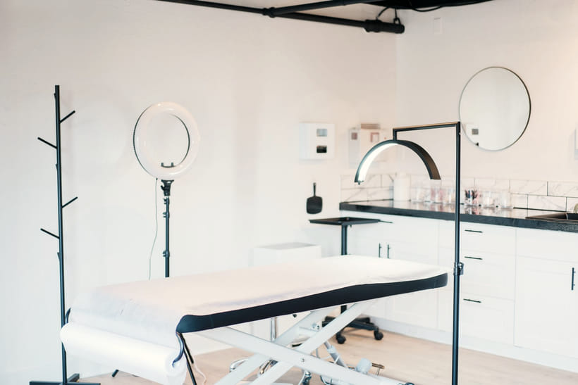 An empty treatment room with a made-up bed, ring light and a clear worktop