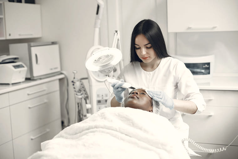 A clinician works under a magnifying lamp during a facial skin treatment